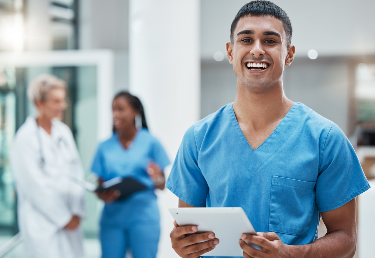 A nurse smiling and holding a tablet in a medical facility.