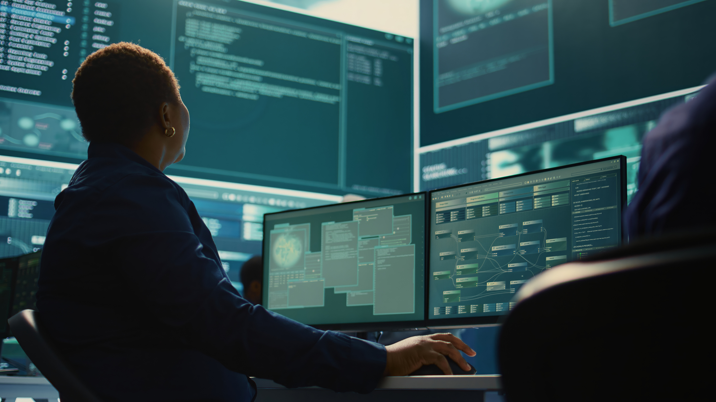 A cybersecurity professional working on two monitors in a control room.