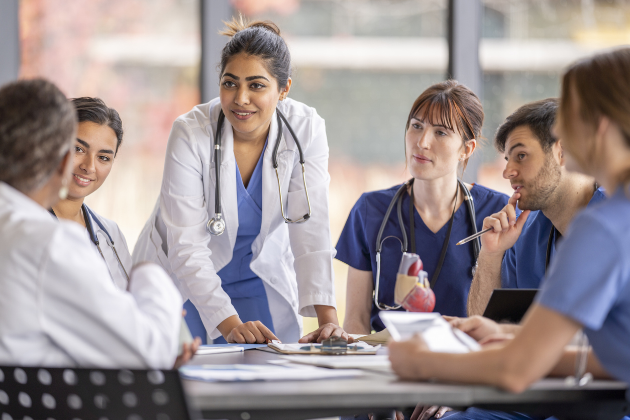 A Nurse Leader in a White Coat Leads a Discussion Around a Conference Table