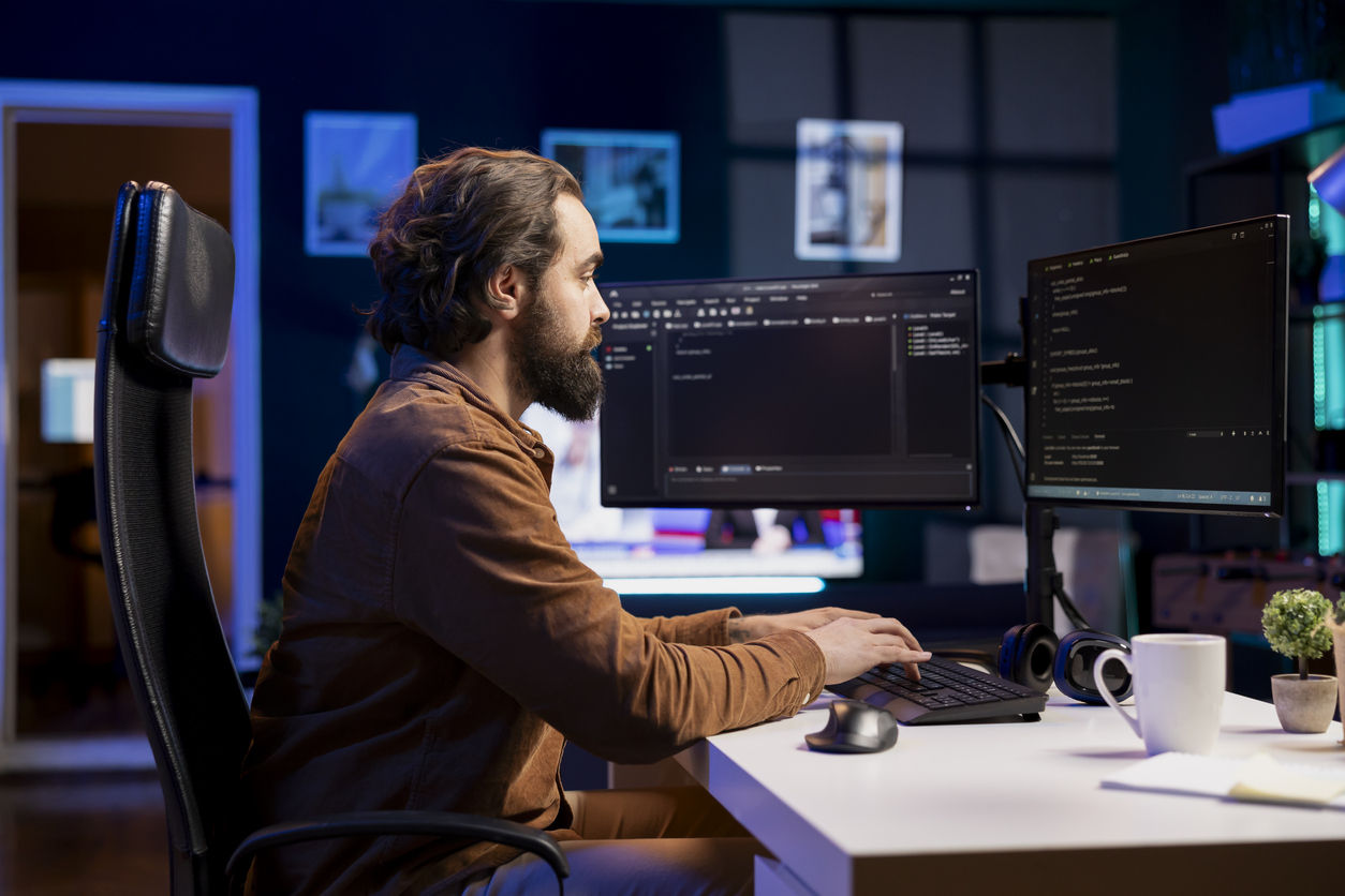 A malware analyst types on a keyboard while reviewing code on a pair of monitors.