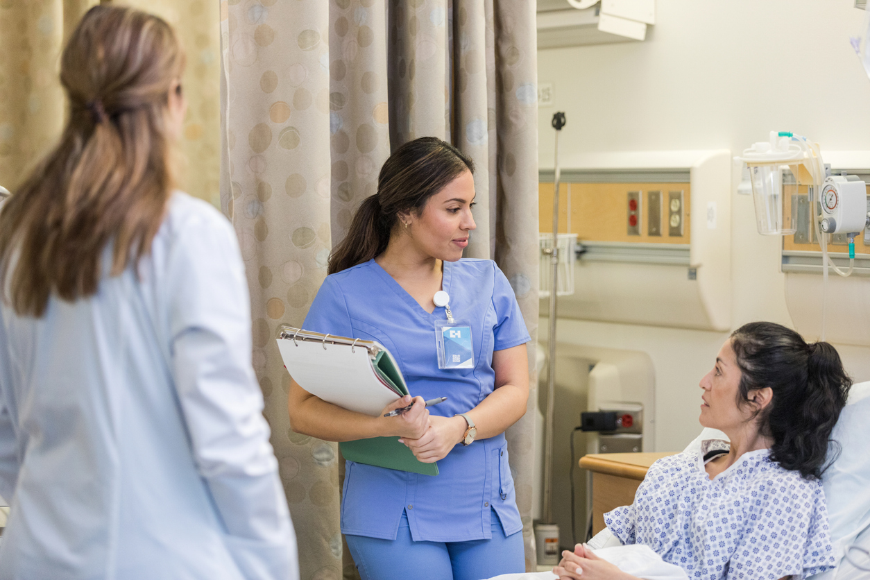 A Nurse in Clinicals With a Clipboard Speaks to a Patient..jpg