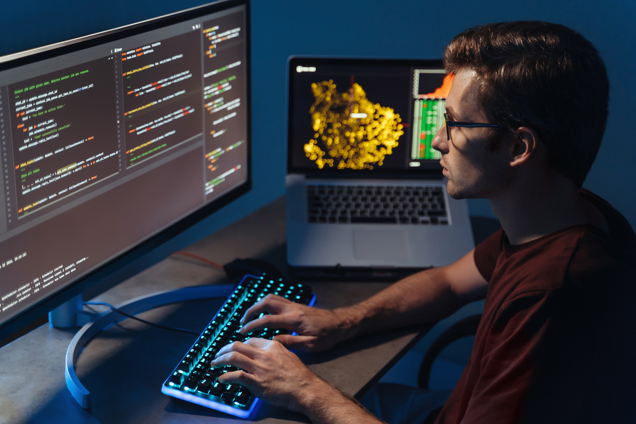 A Cybersecurity Specialist Writing Code Using a Keyboard and Multiple Computer Screens.