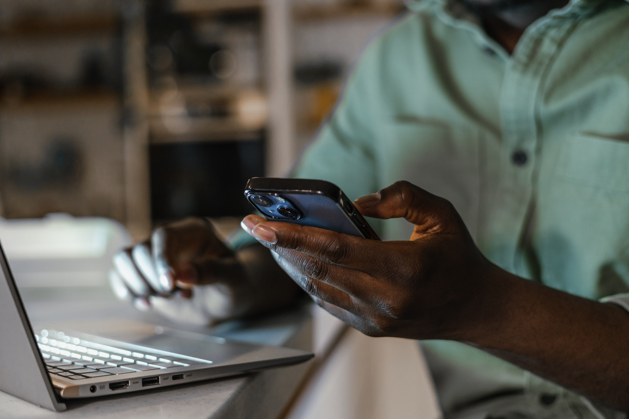 A close-up of a person’s hands using a laptop and a smartphone at the same time.