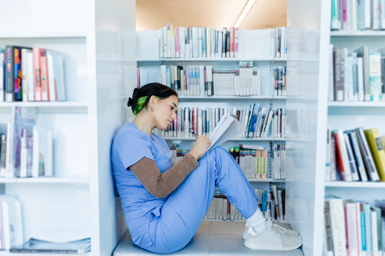 A Nurse Wearing Scrubs Marks up a Document While Sitting in a Library..jpg
