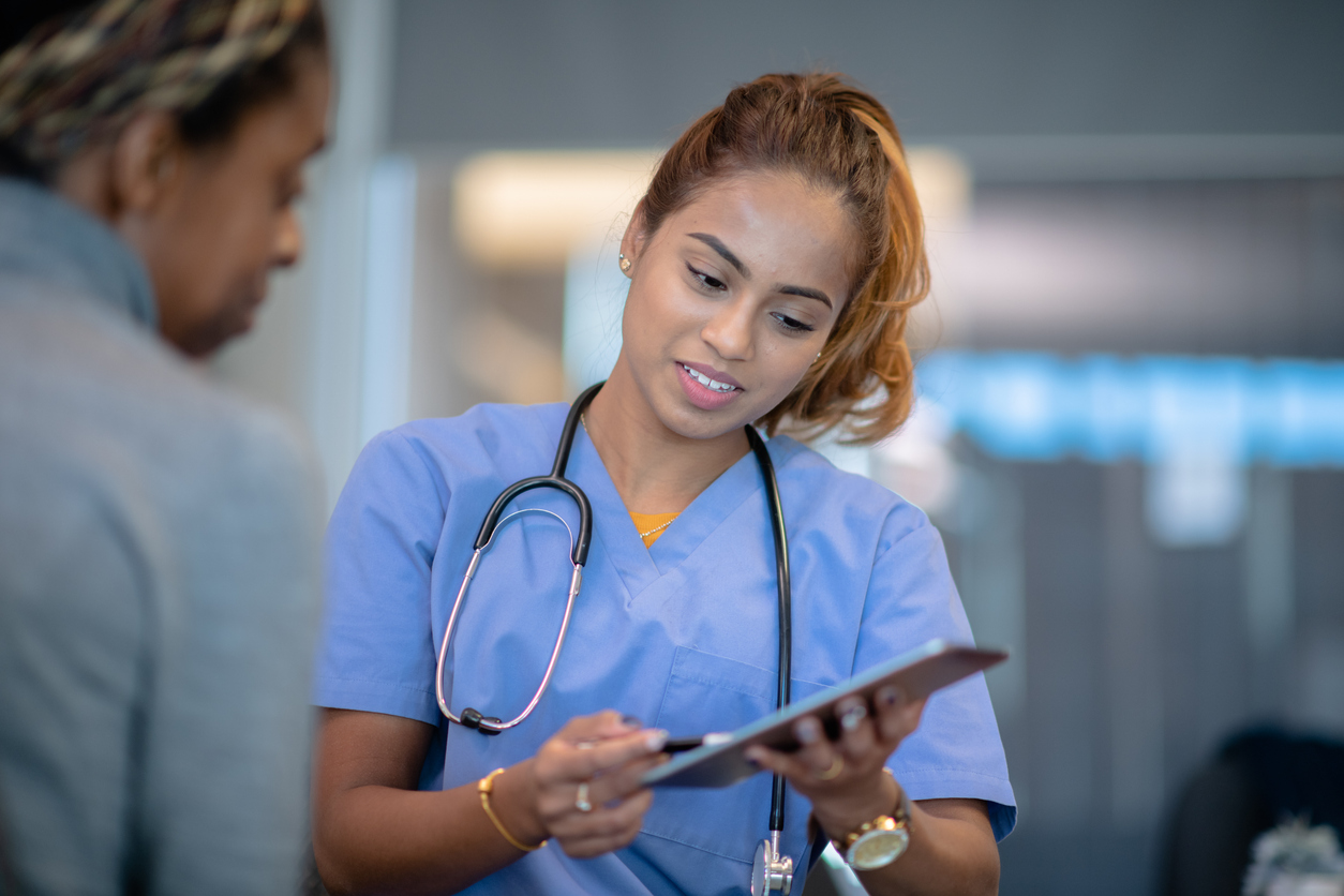 Nurse Manager Talking With a Patient and Pointing to Something on a Clipboard.
