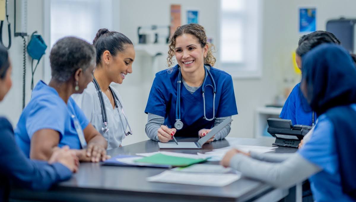 A smiling group of nurses meets around a conference table.