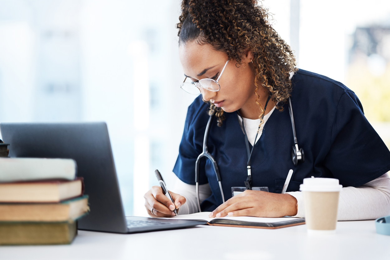 Nursing student in scrubs working on a laptop.